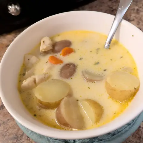 Image shows a close up of a white bowl filled with Cajun potato and chicken soup. There's a spoon in the bowl.