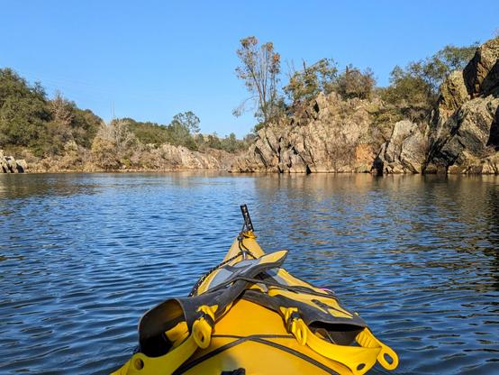 The nose of my yellow kayak looking over the American River at some nice rock formations along the shore.
