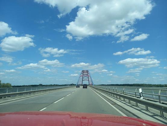 Die Brücke auf der B 191 ist ein Bogen aus Stahl, gestrichen in den Farben blau und rot. Ich knipse vom Beifahrersitz aus, vor uns sind zwei Fahrzeuge. Der Himmel ist überwiegend blau mit ein paar weißen Schäfchen-Wolken.