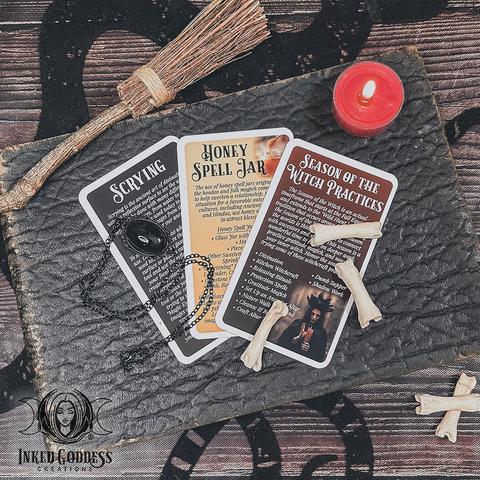 A set of 3 cards are arranged on a leather-bound book. Each card in the "Season of the Witch Eclectic Witch Card Expansion Pack" features information on some of the Samhain magick you can try, including Scrying, Honey Spell Jar, and general Season of the Witch Practices. This is an exclusive product from Inked Goddess Creations.