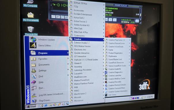 Windows 98 desktop with the Start menu open, showing a list of installed programs. The 'Creative' folder is highlighted, revealing software like Creative PlayCenter 2.0, Creative WaveStudio, Sound Blaster Live!, and EAX Demo. Winamp is playing a MIDI file, and the background features a fiery 3dfx wallpaper. The screen is displayed on a Samsung SyncMaster 755DF monitor.