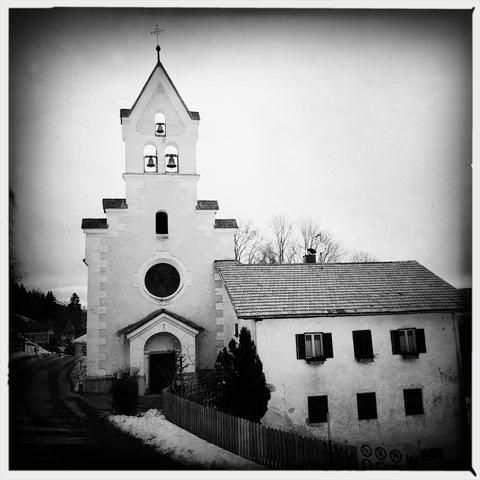 La facciata anteriore del campanile di una chiesa ed una casa vicino alla strada