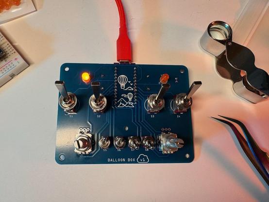 Blue circuit board with switches soldered on. An orange LED in the upper left is lit.
