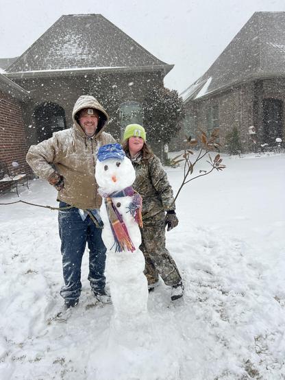 An adult man and child standing next to a snowman.