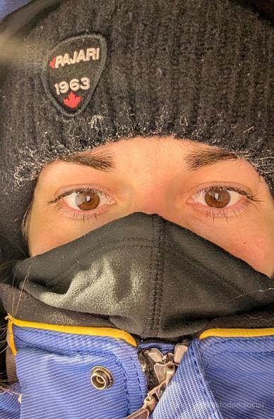 a human face, completely covered in winter clothes, with just the eyes showing. the eyelashes are starting to frost and the brim of the black toque is frosted as well.
