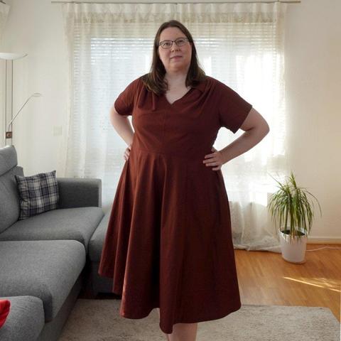 Full body image of a woman in a red dress with circle skirt, short sleeves and gathers at the shoulders.