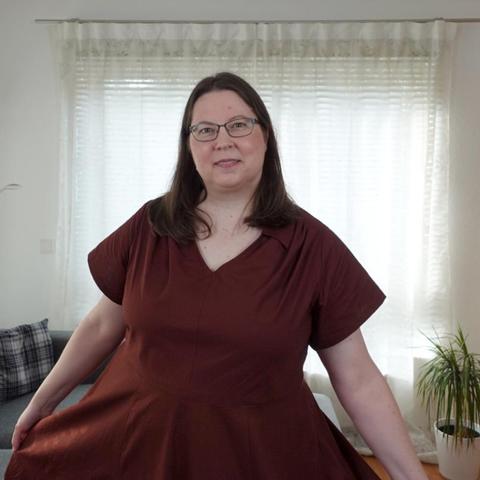 Close up of a woman in a red dress with circle skirt, short sleeves and gathers at the shoulders.