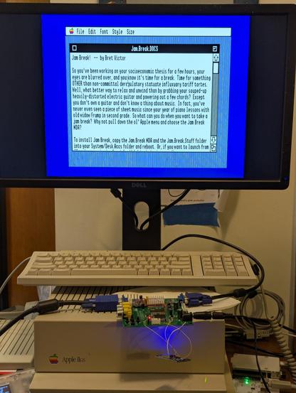 A photograph of an Apple IIgs computer.  A GBS-C upscaler is laying precariously on top of the computer itself.  The display shows the document "Jam.Break.DOCS" open in the Teach text editor.  The picture is very clean and stable.
