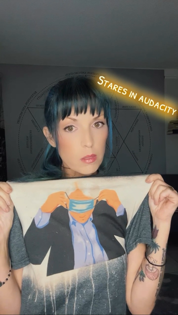 Woman offerings stern look while holding up a shirt featuring Senator Jim Justice struggling to figure out how his face mask works. 