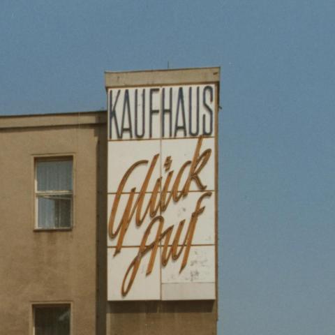 Das Bild zeigt einen Ausschnitt des Gebäudes, in welchem sich derzeit die Universitätsbibliothek Chemnitz befindet. Früher war in diesem Haus das "Kaufhaus Glück Auf", dessen Werbeplakat auf dem Foto abgebildet ist.