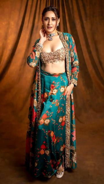 In her latest appearance, Pragya Jaiswal dons a mesmerizing traditional ensemble designed by Ritu Kumar. The outfit includes a golden embroidered crop top, a vibrant floral teal skirt, and a matching jacket with detailed golden embroidery. Paired with a sleek low ponytail and soft smoky makeup, Pragya exudes elegance and sophistication, making this look a must-see for fashion enthusiasts.