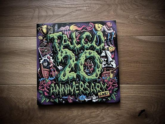 Das Album von Talco ist im bunten Comic-Stil gehalten, die Überschrift Talco 20 Anniversary ist grün, das Album liegt auf Holzplanken.