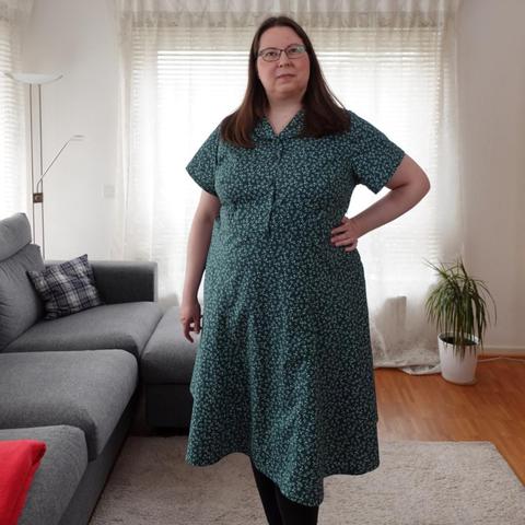 Full body view of a woman in a green dress with leeves pattern, short sleeves and collar.