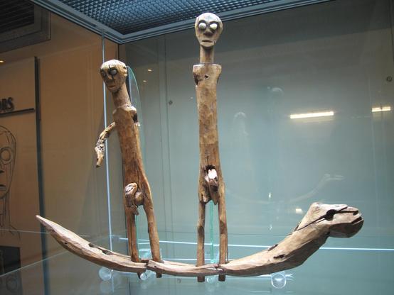 Dos figuras de madera, alargadas, a la que les queda un solo brazo, sobre una barba que tiene agujeros para 8 piernas. Los genitales se pueden retirar e intercambiar.
