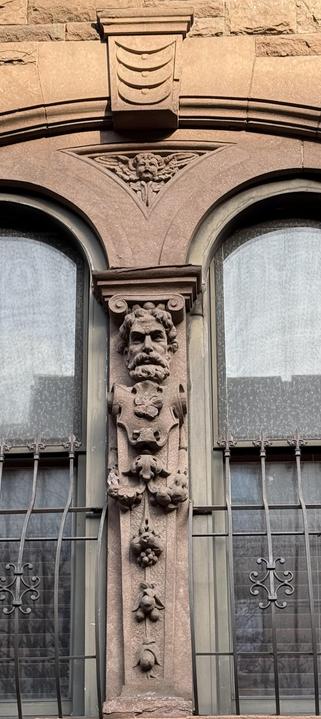 A photo of two window flourishes, a cherub and a watcher figure on an upper west side brownstone. 