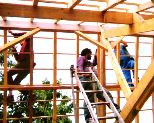 Une photo de chantier sur une charpente avec les travailleurs perchés dans la charpente, Pascal MOREL, gérant de J.M.B. Construction, est perché au centre.