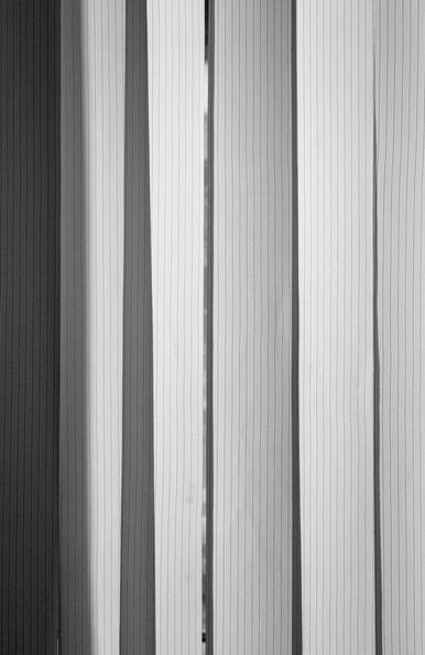 The black-and-white photo shows blinds, some of which are illuminated by the sun, some in the shade. This creates a rhythm, a kind of graphic pattern.
