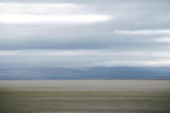 Fotografía en la que se ve un paisaje borroso por el movimiento intencionado de cámara donde la tierra, algunas montañas lejanas y una gran porción de cielo se emborronan en capas al estilo un poco pictórico.