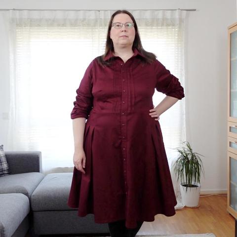 Full body image of a woman in a red dress with button down collar and pintucks in the bodice, long sleeves and a circle skirt with tucks.