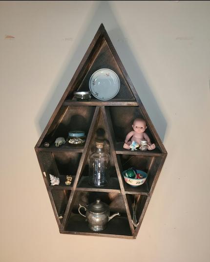 Dark-brown, geometric wall shelf with decorative items, including small figurines, animal bones, a jar of cat whiskers, pocket knives, small pool balls, and a silver tea pot container.