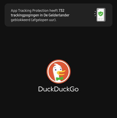 Tekst bovenin: "App Tracking Protection heeft 732 trackpogingen in De Gelderlander geblokkeerd (afgelopen uur)." met rechts daarvan een geïlustreerd telefoontje met daarin een groen harnasje met een 'v' symbool.

In het centrum van de abeelding het logo van DuckDuckGo: een geïlustreerde kop van een wit lachend eentje met oranje snavel en groene vlinderdas.

De achtergrond van het screenshot is geheel zwart
