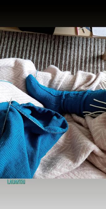 Sininen villasukka ja sininen neulepaita puikoilla.