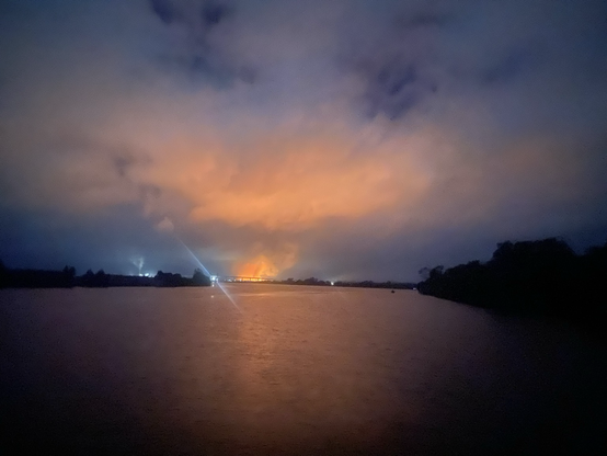 Photo from house boat on Clarence river NSW centre of the image is a burning sugar cane fire, casting a red glow on the surface of the river. The red orange colour is reflected onto the clouds with an attractive blue thrown at the horizon and the corners of the image. Looking at the Harwood bridge and sugar can