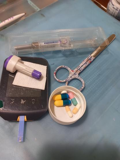 Appareil à glycémie, médicaments dans un bouchon, paire de ciseaux et injection posée au-dessus