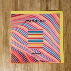 Das Albumcover ist überzogen von vielen farbigen Streifen in rot, Petroleum, gelb und apricot. Außen eine gelbe Umrandung. Das Album liegt auf dem Holzboden.