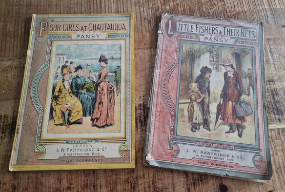 Two pansy magazine books with beautiful coloured covers with women on them, dressed like they did before 1900, carrying umbrella's. The more yellow magazine is 'Four girls at Chautauqua' with five illustrations. The more pink one is 'Little fishers and their nets' with seven illustrations. 
