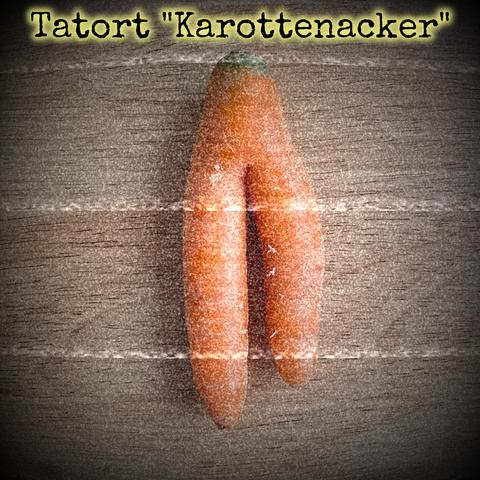 Eine zweigeteilte Karotte liegt auf einer Holzplatte. Verrauschtes Foto.
Text: Tatort "Karottenacker"