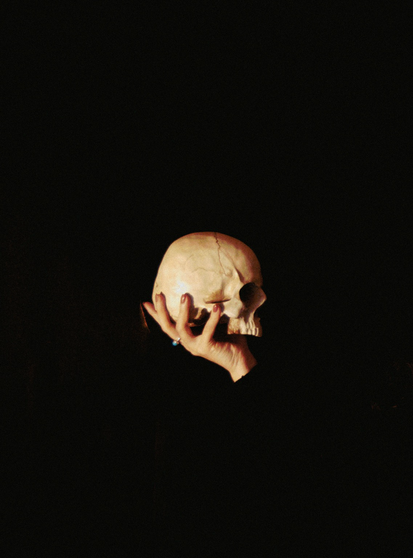 A dimly lit composition of a hand delicately holding a human skull against a dark, almost black background, evoking themes of mortality and contemplation.