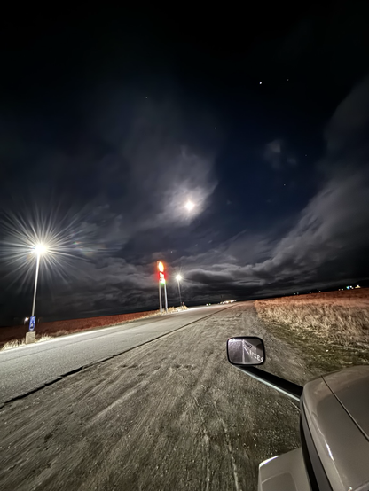 Dark night with clouds and a full moon, gas station sign and street light off the freeway on ramp