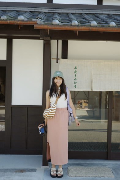 A girl standing in front of a traditional japanese store smiling and posing for the photo. The store seems to be in a traditional wodden building and is located in Uji, Japan.