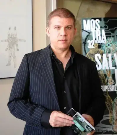 Photo de Salvador Larroca posant devant un poster et un dessin. Il porte une veste sombre rayée.