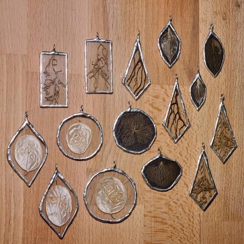 Some handmade stained glass pendants. Between the glass planes are lunaria discs, plants roots, skeleton leaves and hydrangea petals. The latter have a black background so they stand out more on the skin.