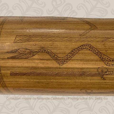 Un détail d’un bambou gravé kanak, mettant en évidence un serpent finement dessiné, au corps orné de points réguliers et d’un motif géométrique. Le serpent est entouré de lignes parallèles gravées. Photographie réalisée par Éric Dell'Erba, pour la collection du musée de Nouvelle-Calédonie.