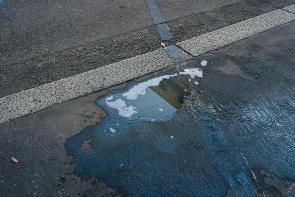 A soapy puddle on the sidewalk reflecting a yellow building and some blue sky