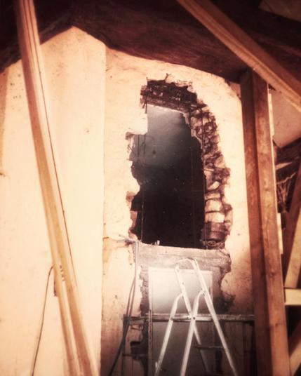 Une ouverture en hauteur réalisée dans le mur, avec une porte en dessous et l'escabeau devant. Il y a des poutres en bois foncé visibles sur le côté et au plafond.