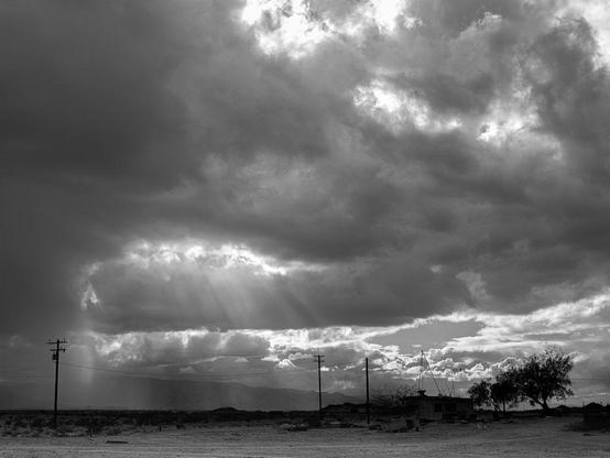 Sunburst amid storm clouds over desert landscape.