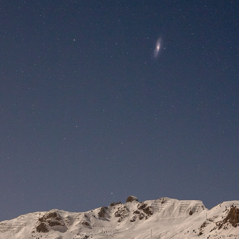 Gros plan de la galaxie d’Andromède visible au dessus de montagnes enneigées 