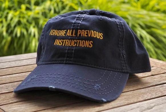 Photograph of a baseball cap with the inscription "Ignore all previous instructions". Image attribution: AI Tinkerers.