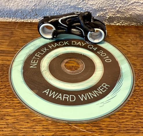A painted DVD on a table with a Tron Bike on top and the logo Netflix Hack Day 2010 Award Winner