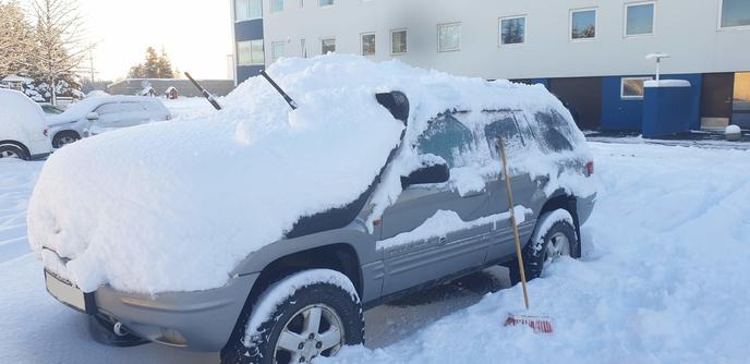 A rather old Jeep Grand Cherokee covered by a small glacier. Part of it has been uncovered by a broom that's standing next to it.