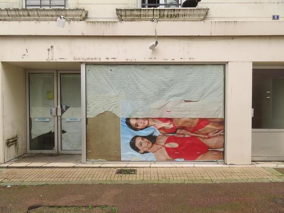 une vitrine à moitié occultée. Dans la partie basse une grande image à l'horizontale d'Alerte à Malibu, 2 femmes en maillots de bain rouges