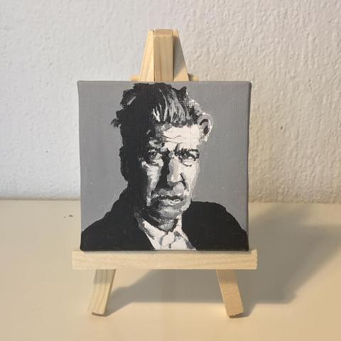 A black and white portrait (7 by 7 cm) on an easel, of a person looking rather sternly at the viewer