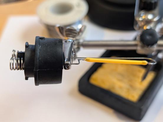 LED light element with broken soldered connection clamped in "third hand" soldering holder.