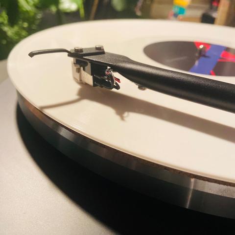 Auf dem Bild ist der Ausschnitt eines Plattenspielers zu sehen mit dem aufgelegten Album in hellbeigefarbenem Vinyl 