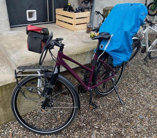 A dark purple bike with a baby carrier covered with a blue cover