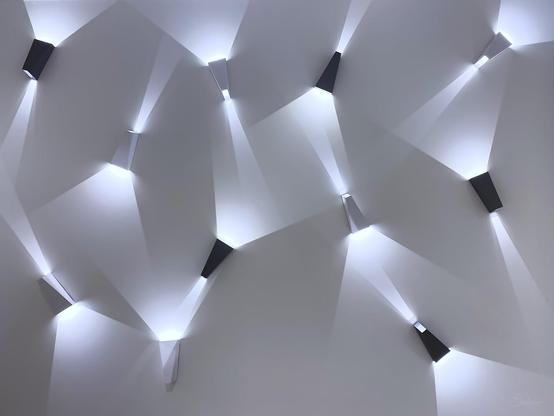 Photo of 10 geometrically shaped lamps on a white wall. The lights and shadows create an interesting and playful pattern